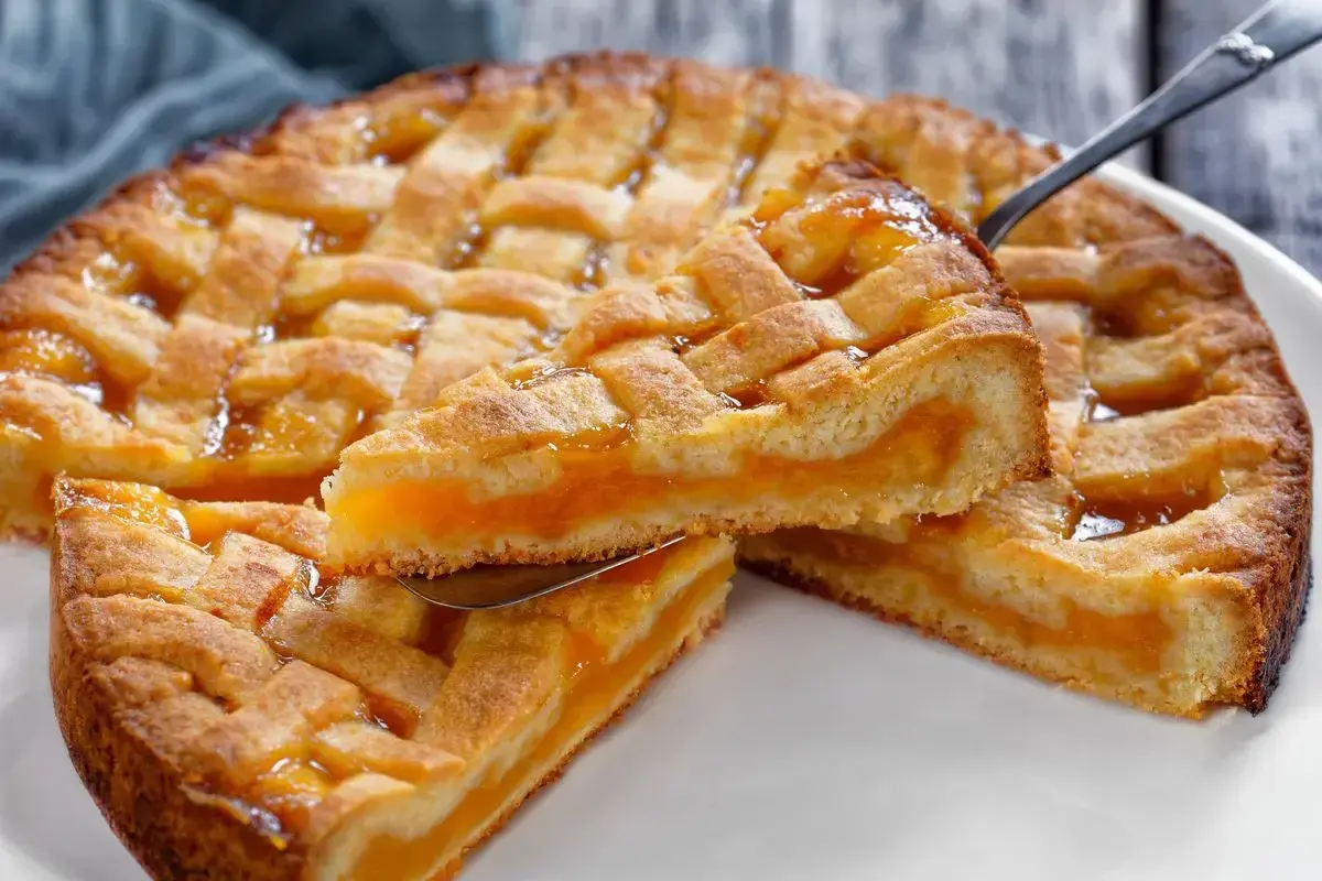 Deliziosa crostata senza glutine con ripieno di albicocche, una fetta sollevata da un coltello.