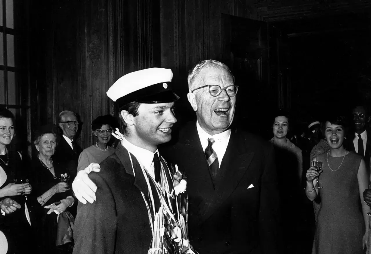 Kung Gustav VI Adolf ler glatt bredvid en student med studentmössa.