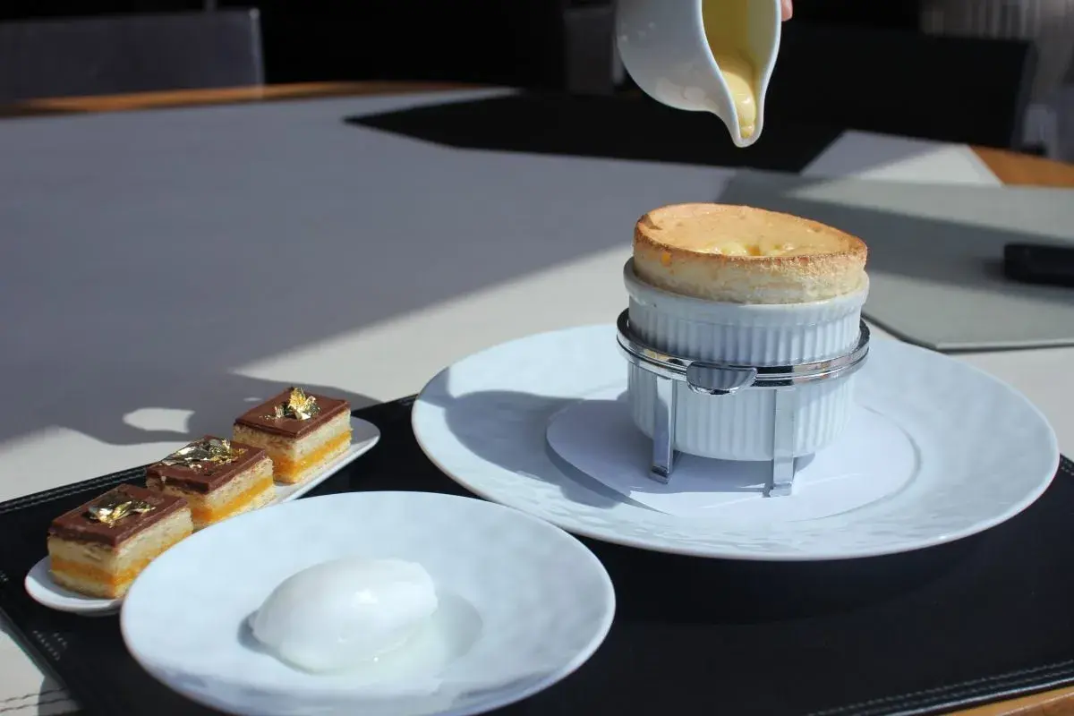 Un délicieux soufflé au Grand Marnier, encore chaud, est servi avec une crème anglaise. À côté, des petits gâteaux au chocolat et une boule de sorbet.