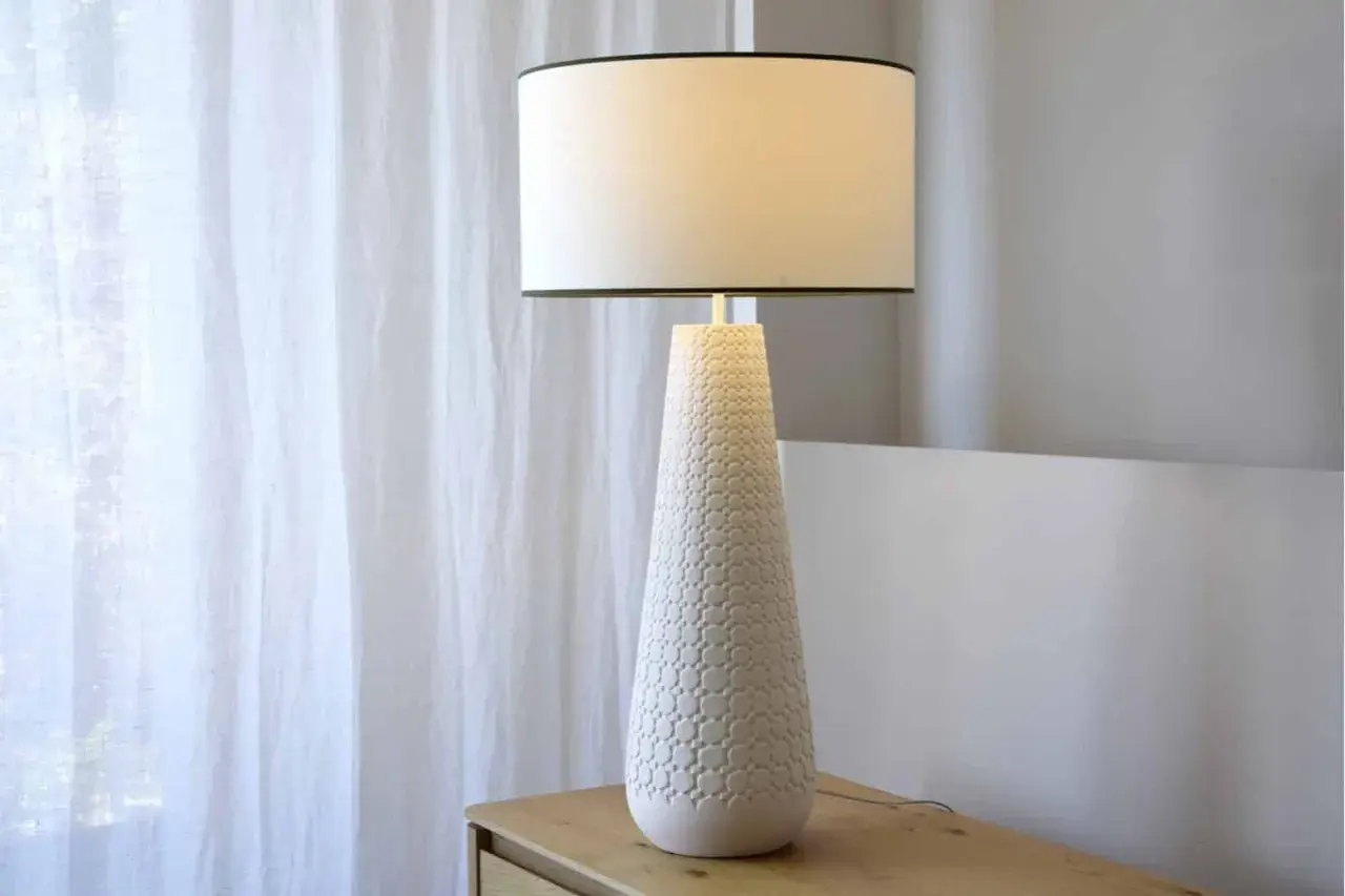 Elegante lámpara de mesa cerámica con base cónica texturizada y pantalla blanca, ideal para añadir un toque de estilo.