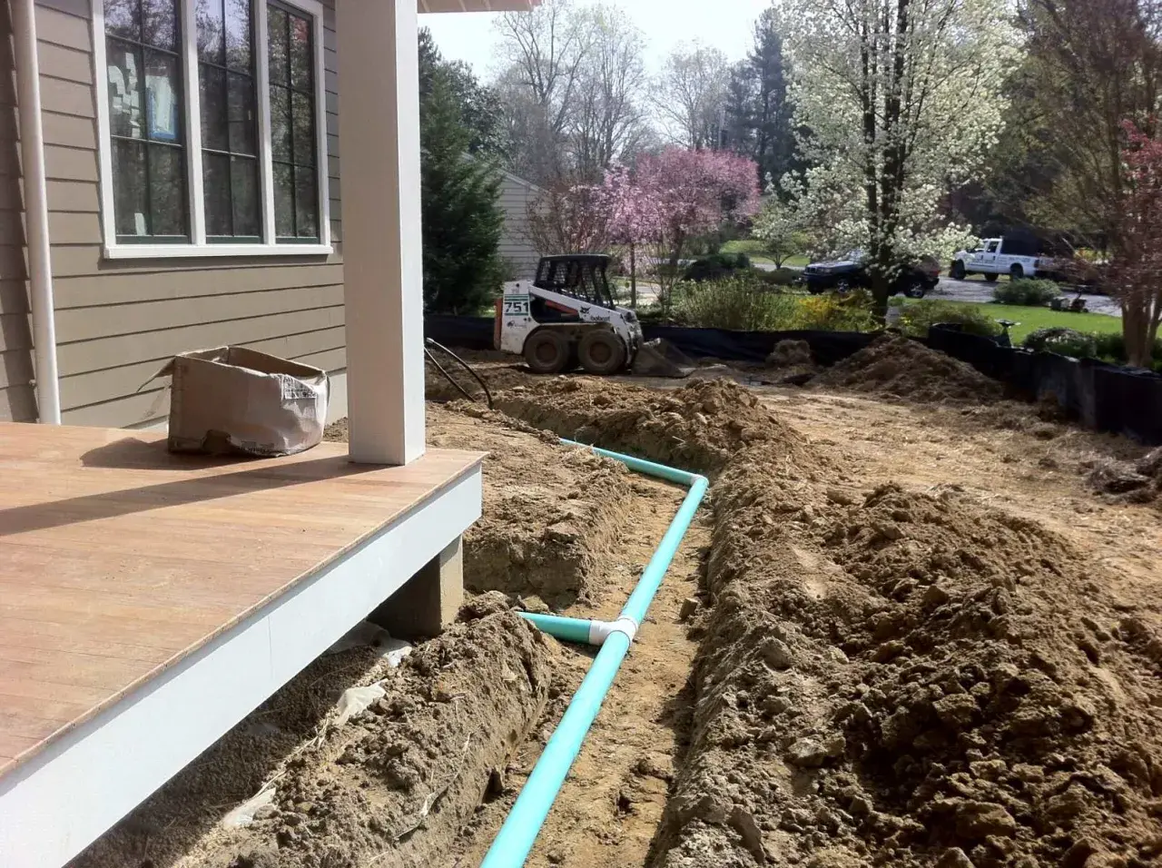 Bauarbeiten am Haus: Ein Bobcat-Lader und ein Bagger sind im Einsatz, um Rohre für die Drainage zu verlegen.
