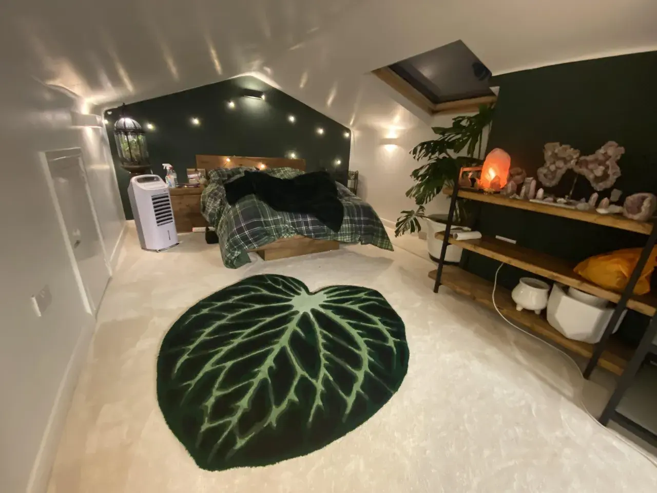 Sovrum med mysig cottage core-känsla. Rutiga sängkläder, gröna väggar och en stor bladmatta. Kristallampor och växter skapar en drömsk atmosfär.