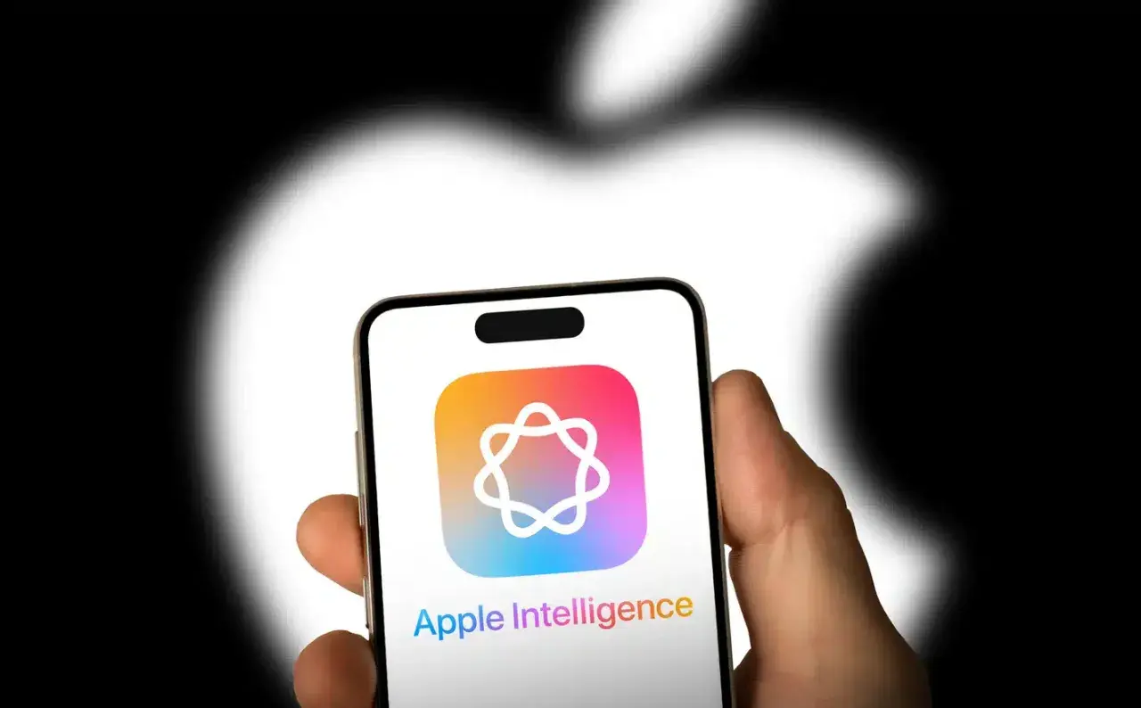 Dłoń trzyma iPhone'a z logo Apple Intelligence. Tło to rozmyte logo Apple.