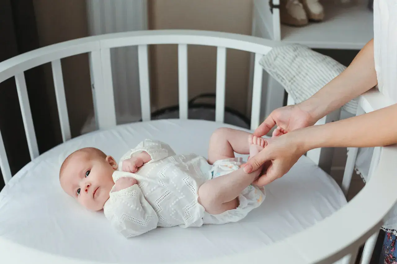 Delikatne nóżki noworodka w białej koronkowej kaftaniku, mama delikatnie je dotyka.