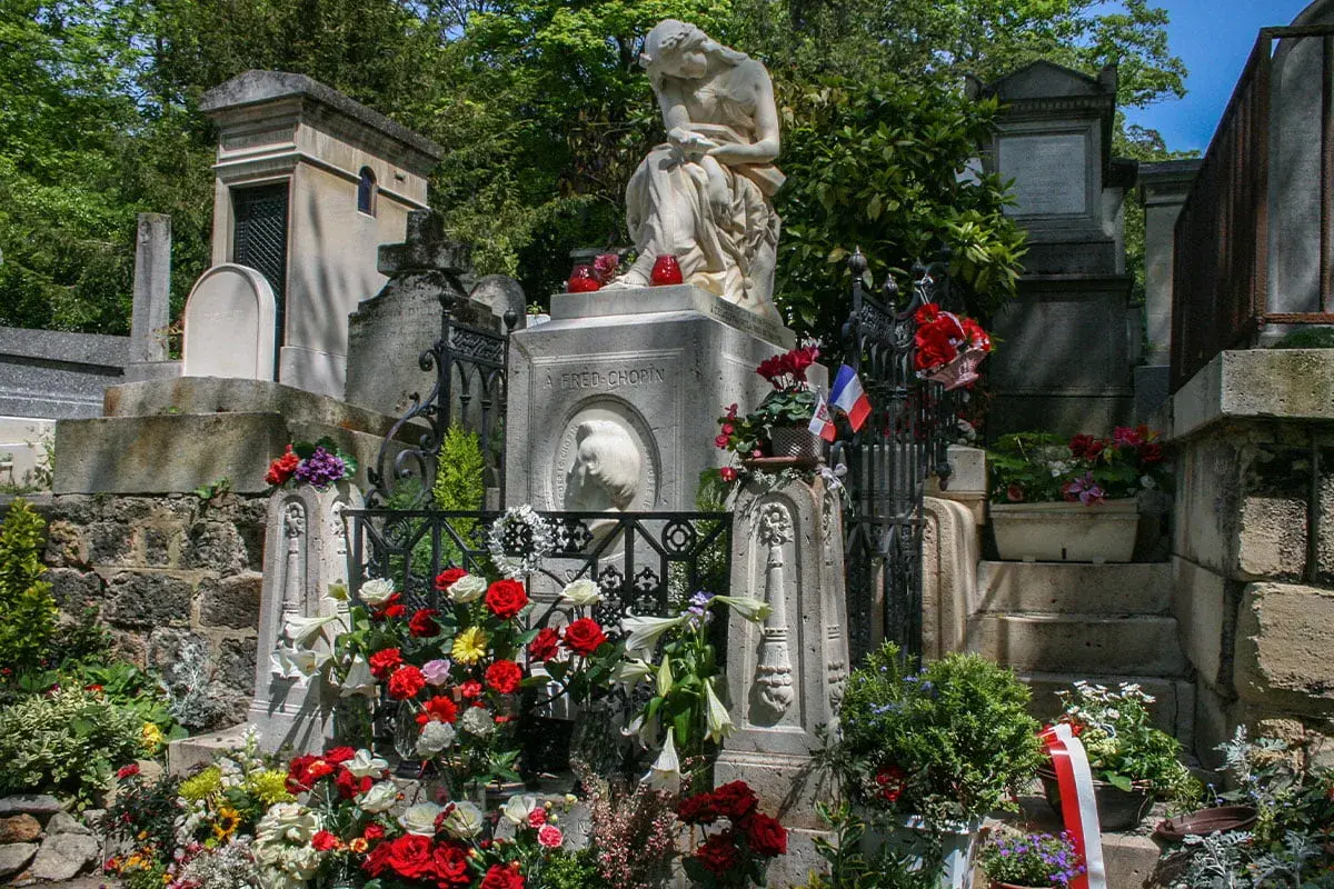 Grób Chopina na cmentarzu Père Lachaise w Paryżu, ozdobiony kwiatami i flagami.
