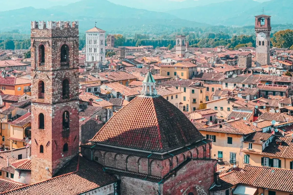 View over a walled city in Tuscany, with terracotta roofs, ancient towers, and distant mountains.