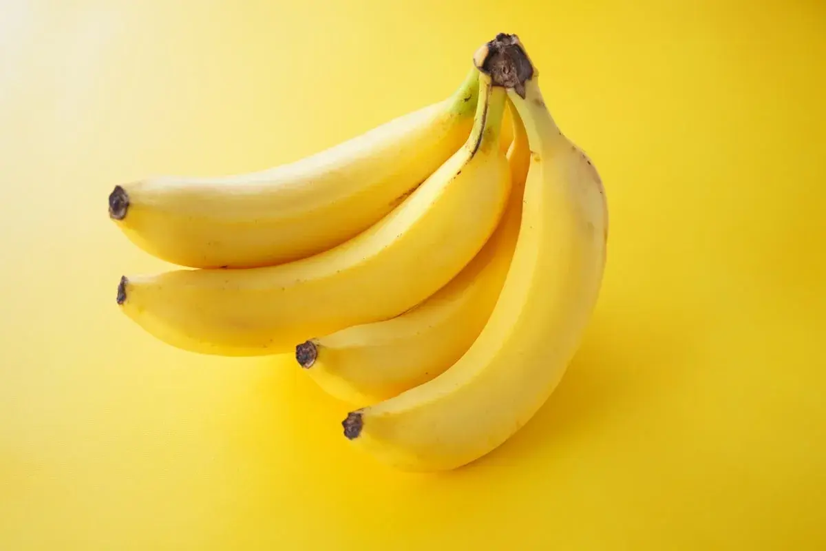 Pęczek żółtych bananów na żółtym tle. Zastanawiasz się, ile kalorii ma średni banan?