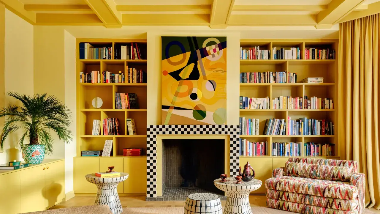 Ein Wohnzimmer in einem gelben Farbrausch, mit Bücherregalen, einem Kamin und einem bunten Sofa.