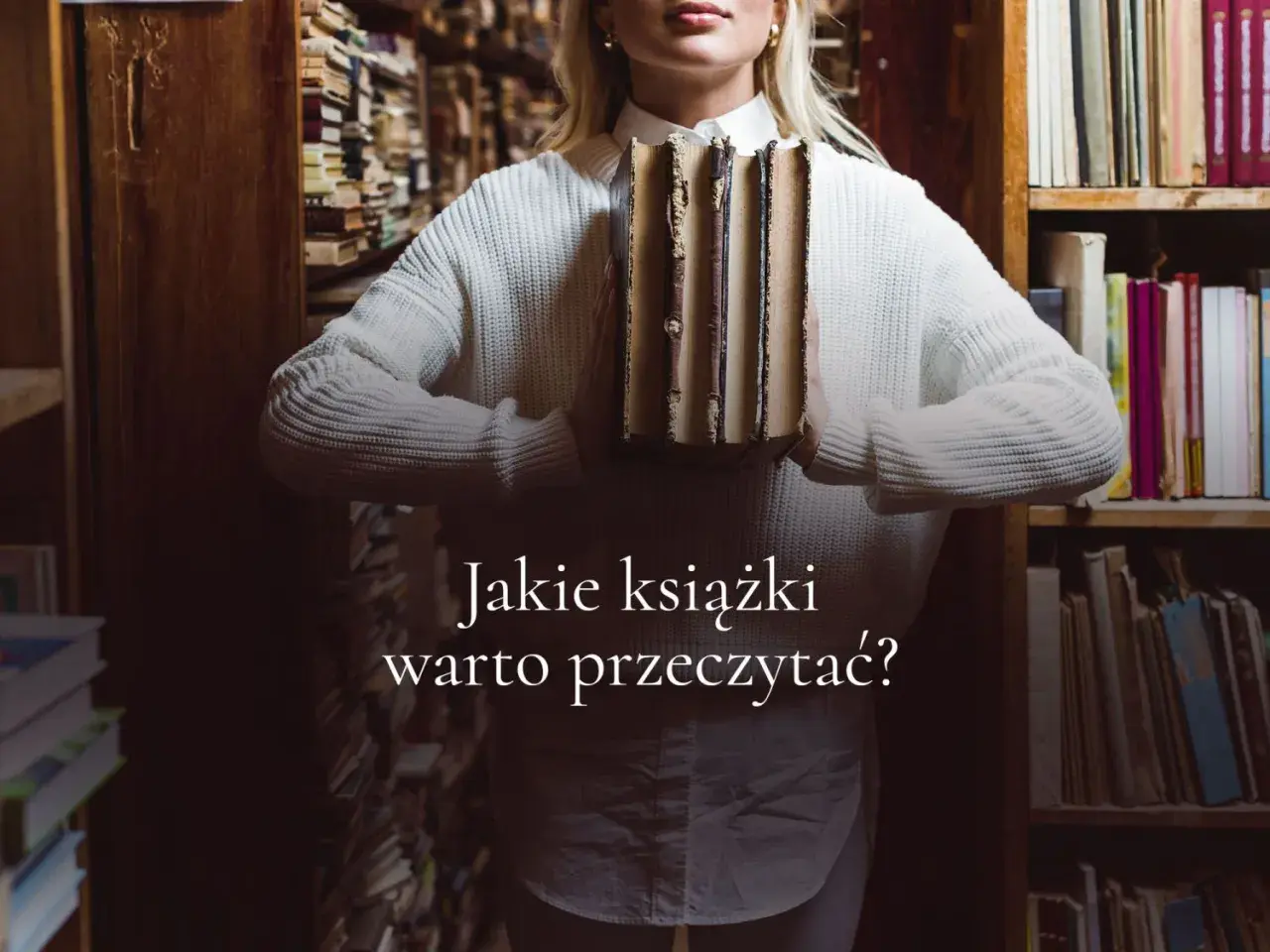 Kobieta w swetrze trzyma stos starych książek w bibliotece. Jakie książki warto przeczytać?