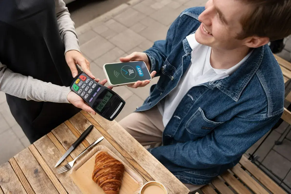 Uśmiechnięty mężczyzna płaci telefonem Santander za croissant. Szybko i wygodnie, jak płacić telefonem Santander.