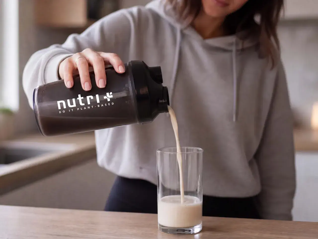 Frau gießt pflanzliches Protein aus einem Shaker in ein Glas. Informiere dich über mögliche proteinpulver nebenwirkungen.