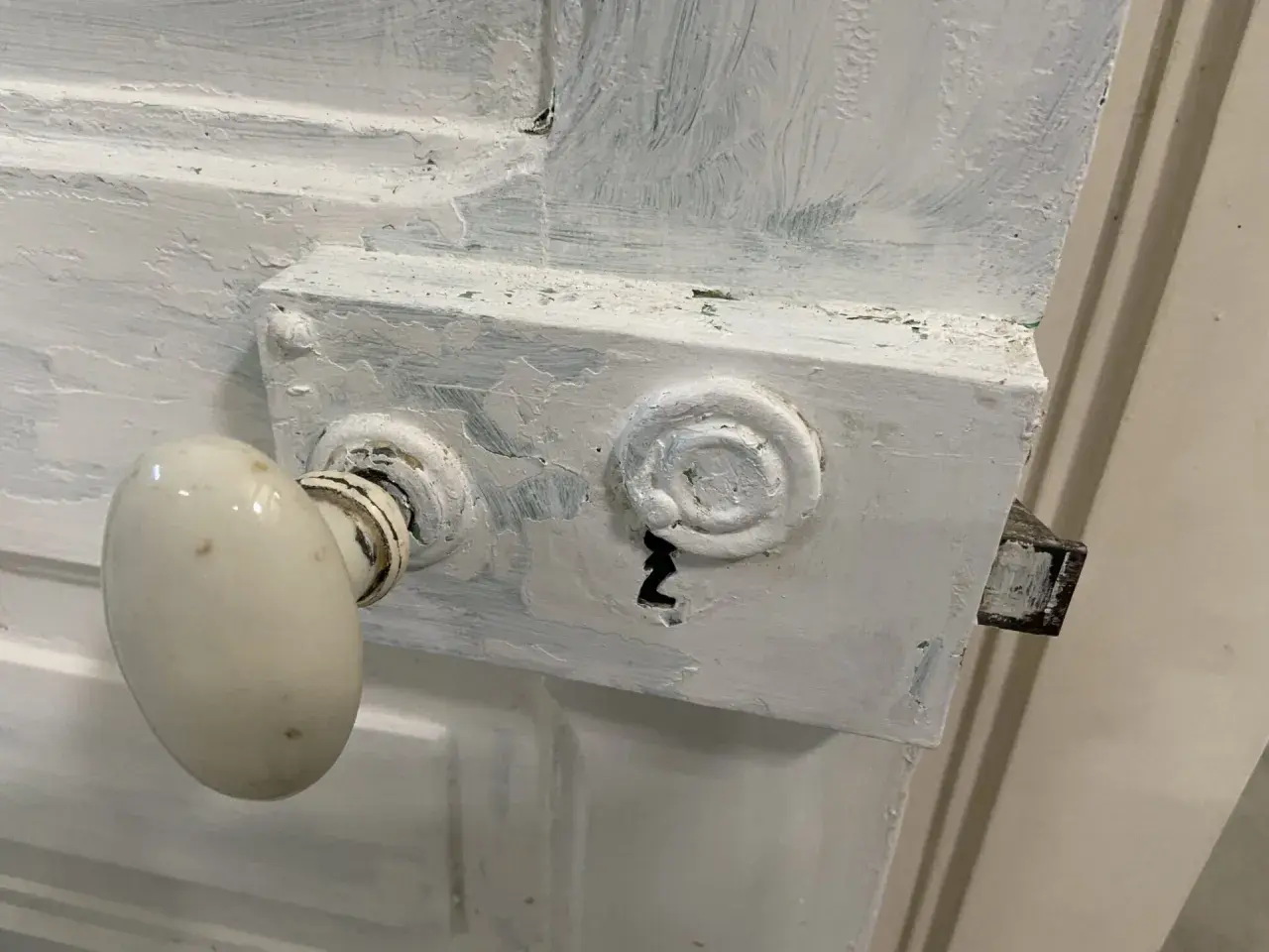 Poignée de porte ancienne recouverte de peinture blanche écaillée. Le mécanisme de serrure est visible, prêt à enlever peinture sur poignée de porte.