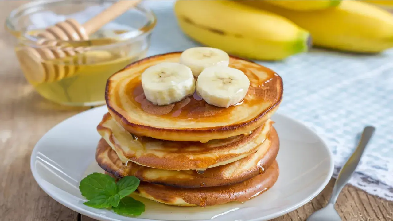 En stapel gyllene bananpannkakor toppas med bananskivor och ringlad honung. Ett enkelt bananpannkaka recept för en härlig frukost.