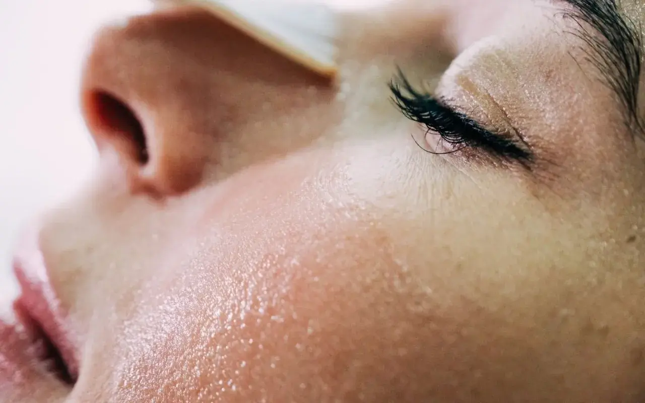 Gros plan sur une peau grêlée, humide et lumineuse, avec un œil fermé et des cils longs.