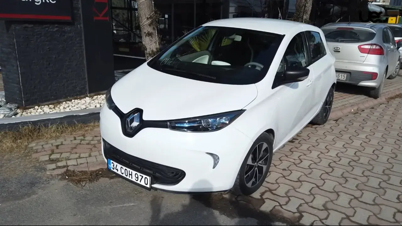 Białe Renault Zoe stoi zaparkowane na chodniku z kostki brukowej.