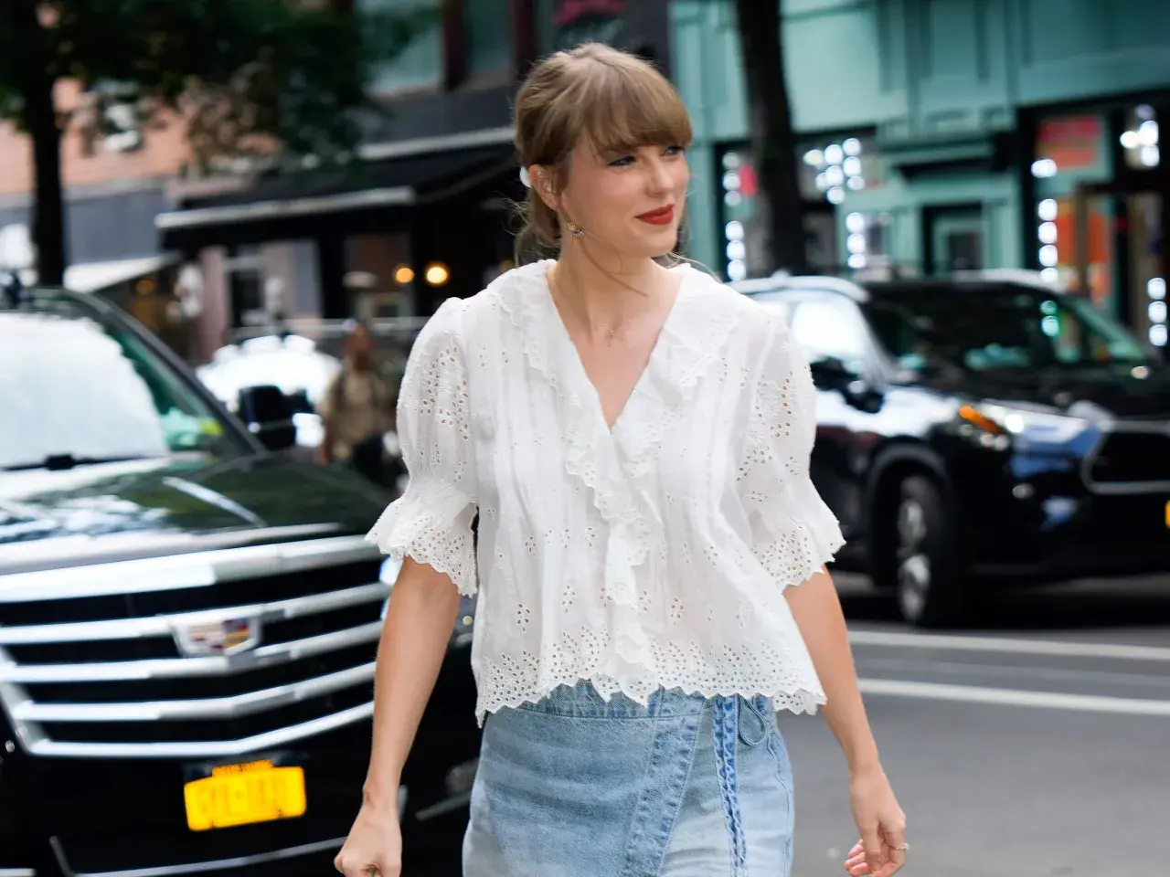 Chica con estilo "clean girl" con blusa blanca bordada y falda vaquera, paseando por la ciudad.