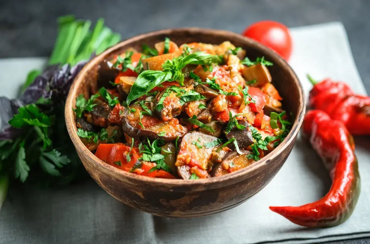 A miseczce caponata siciliana, pełna bakłażana, pomidorów i papryki, ozdobiona świeżą bazylią i pietruszką.