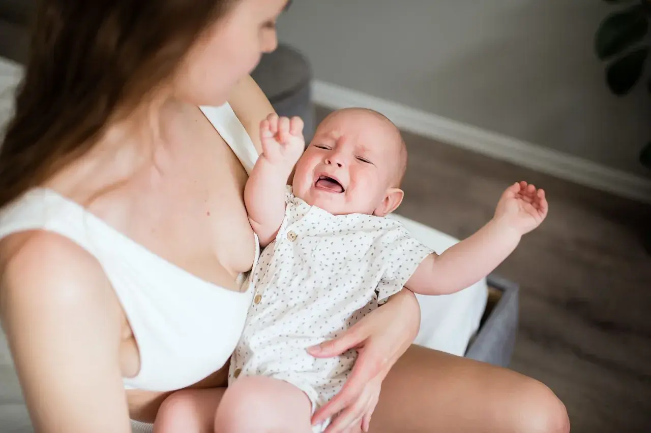 Bambino piange per la dentizione neonato rimedi. Mamma lo culla, cercando sollievo.