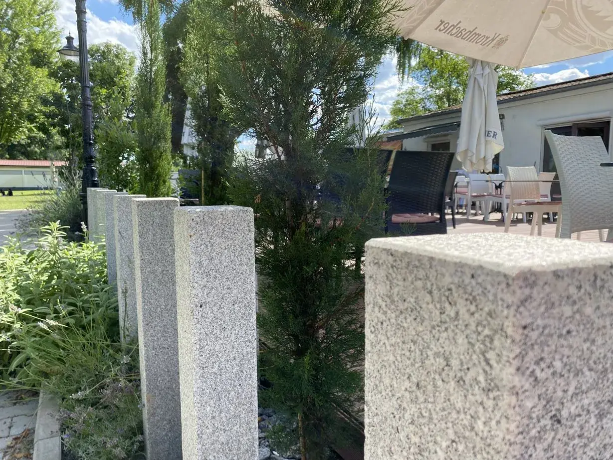 Granit-Palisaden setzen einen eleganten Akzent vor grüner Bepflanzung und laden zum Verweilen auf der Terrasse ein.