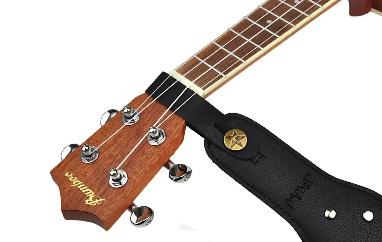 Czarny pasek do gitary zaczepiony na gryfie ukulele. Pokazuje, jak zacząć grać, gdy masz już zamontowany pasek.