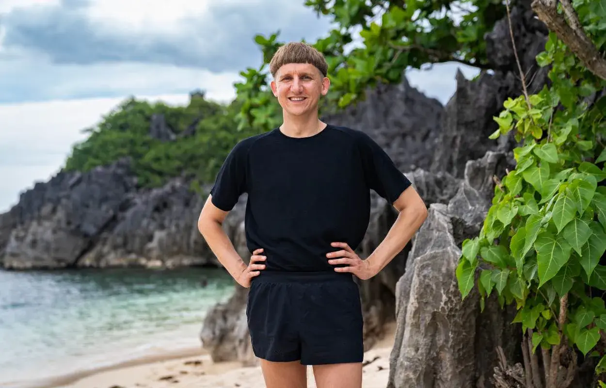 Pål Robinson står på en strand med klippor och grönska bakom sig.