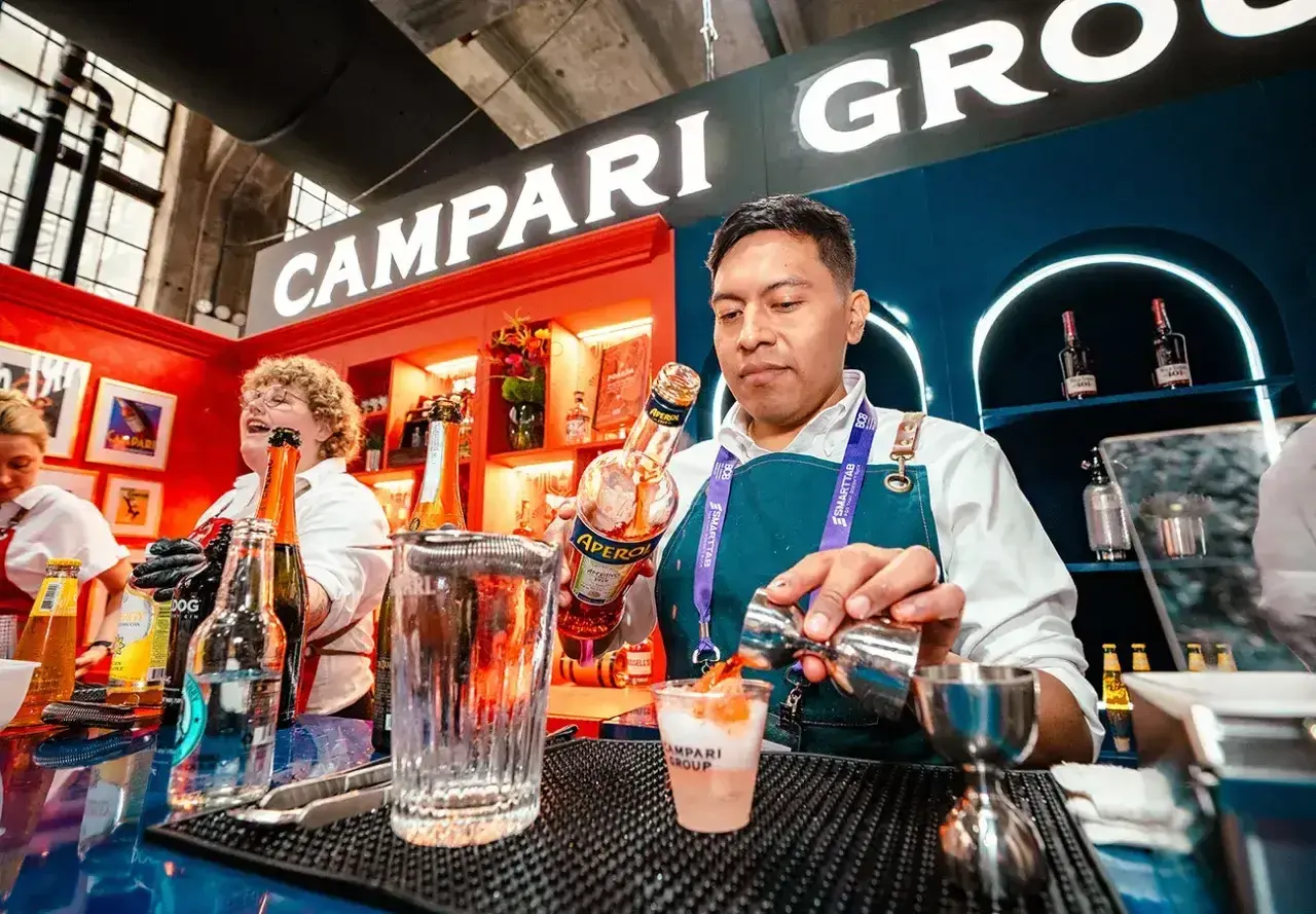 Barman przygotowuje drinka z Aperol. W tle widać logo Campari Group.