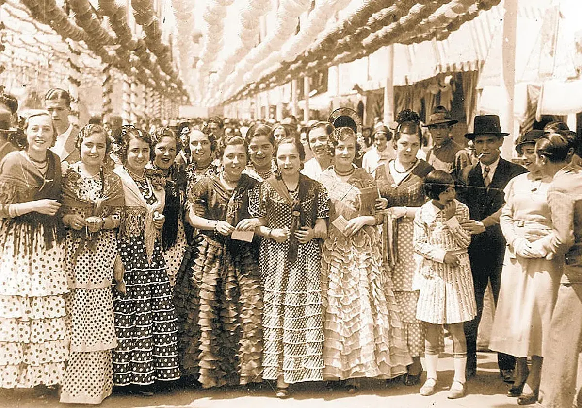 Grupo de mujeres y niñas con trajes de volantes y lunares, evocando el origen del traje de flamenca en una feria antigua.