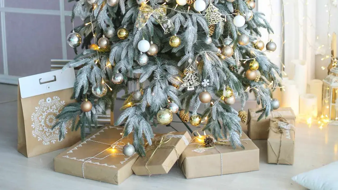 A frosted Christmas tree with gold and silver ornaments, fairy lights, and gifts wrapped in brown paper. Perfect christmas tree decor inspo for a cozy holiday.