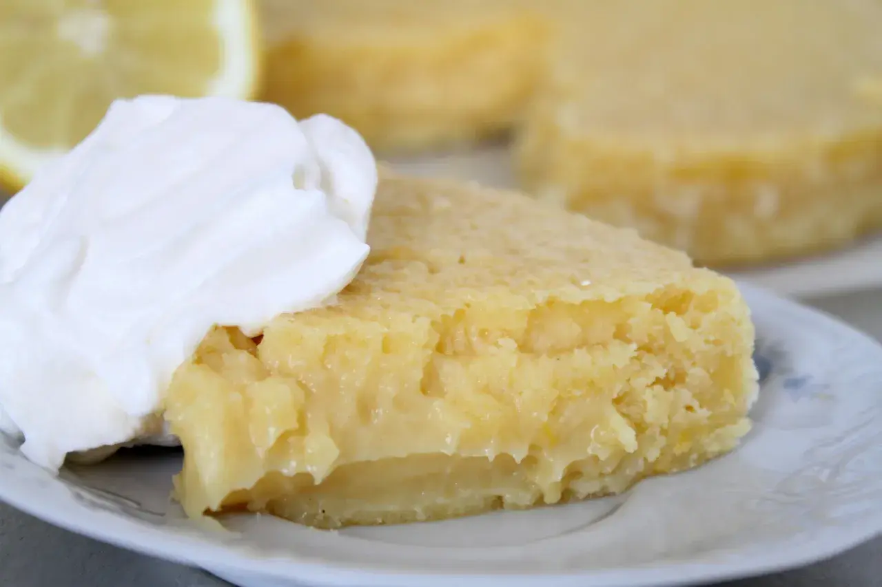 En bit kladdkaka med citron, toppad med vispad grädde. En perfekt citron kladdkaka för fikat.