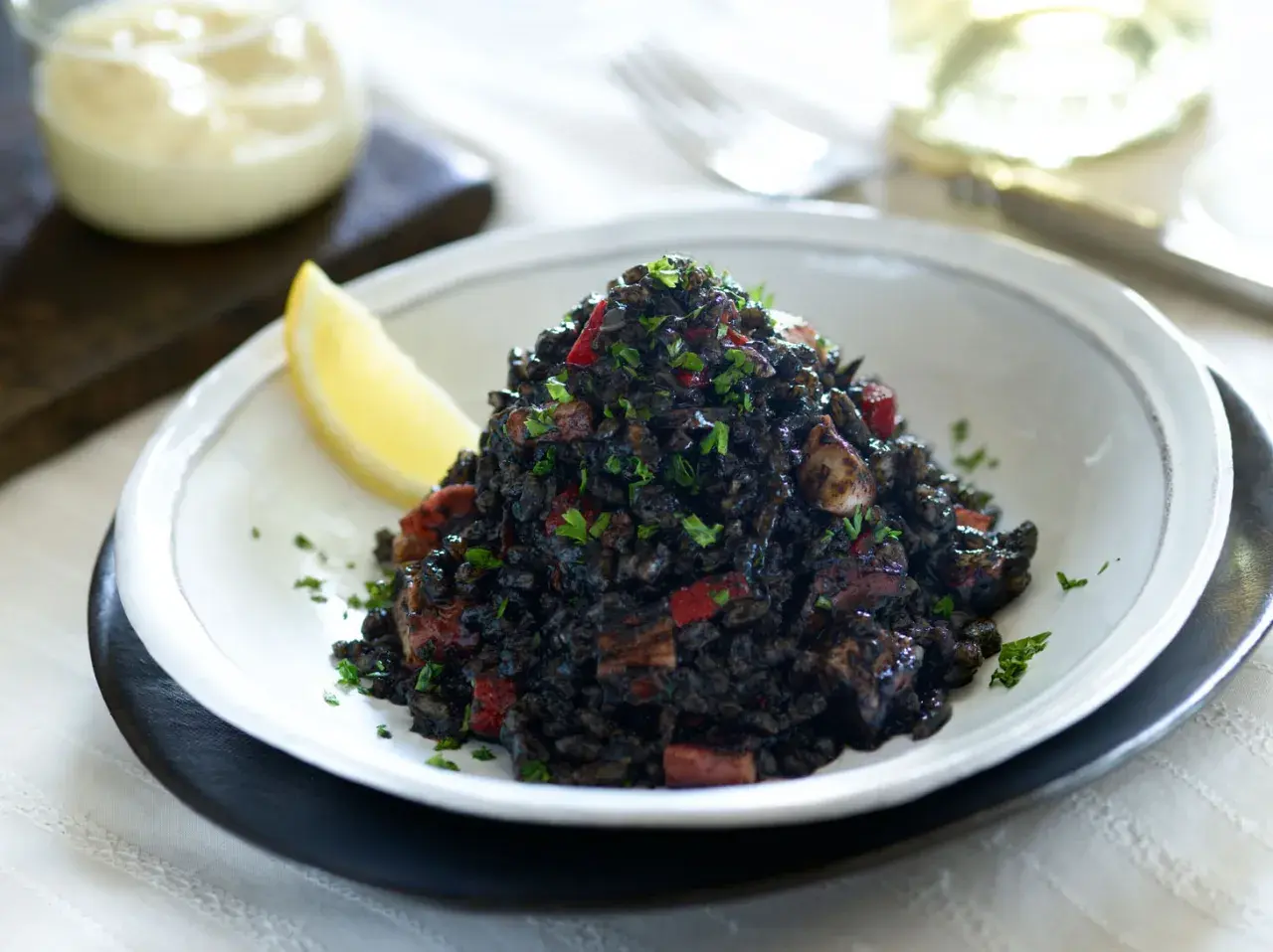 Delicioso arroz negro con trozos de calamar y pimiento rojo, adornado con perejil fresco y una rodaja de limón.