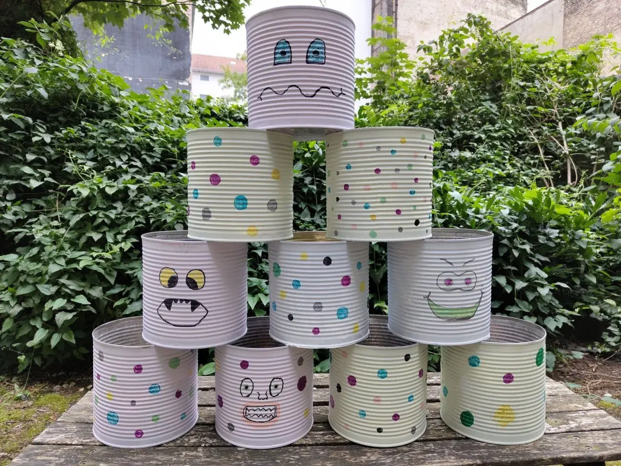 Kreatives Recycling mit Kindern: Dosen-Monster-Turm im Garten. Bunte Punkte und lustige Gesichter machen aus alten Konserven ein Spiel.
