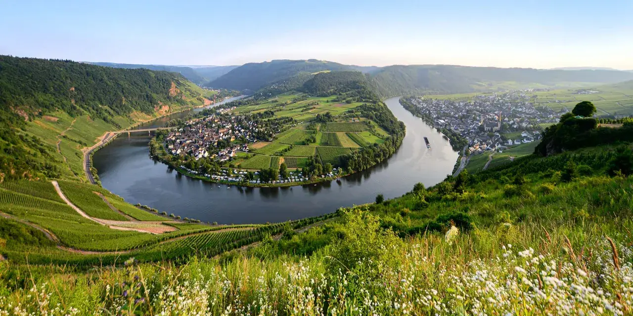 Ein malerischer Flusswindung mit Weinbergen, einem Dorf und einer Brücke. Ein perfektes Beispiel für interessante Reiseziele in Deutschland.