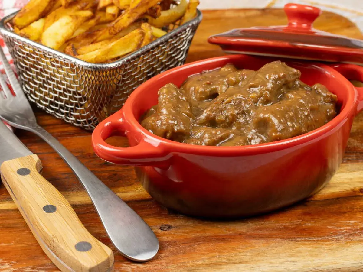 Un plat de carbonade flamande mijotée dans une cocotte rouge, accompagné de frites dorées dans un panier métallique. Un délice réconfortant.