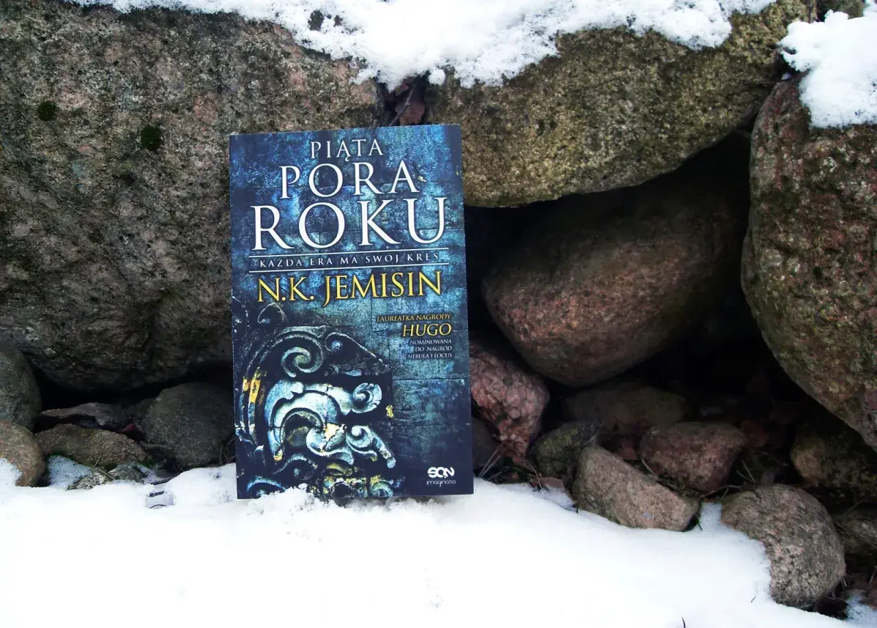 Książka "Piąta pora roku" N.K. Jemisin leży w śniegu między kamieniami. To opowieść o końcu świata, który przychodzi jak piąta pora roku.