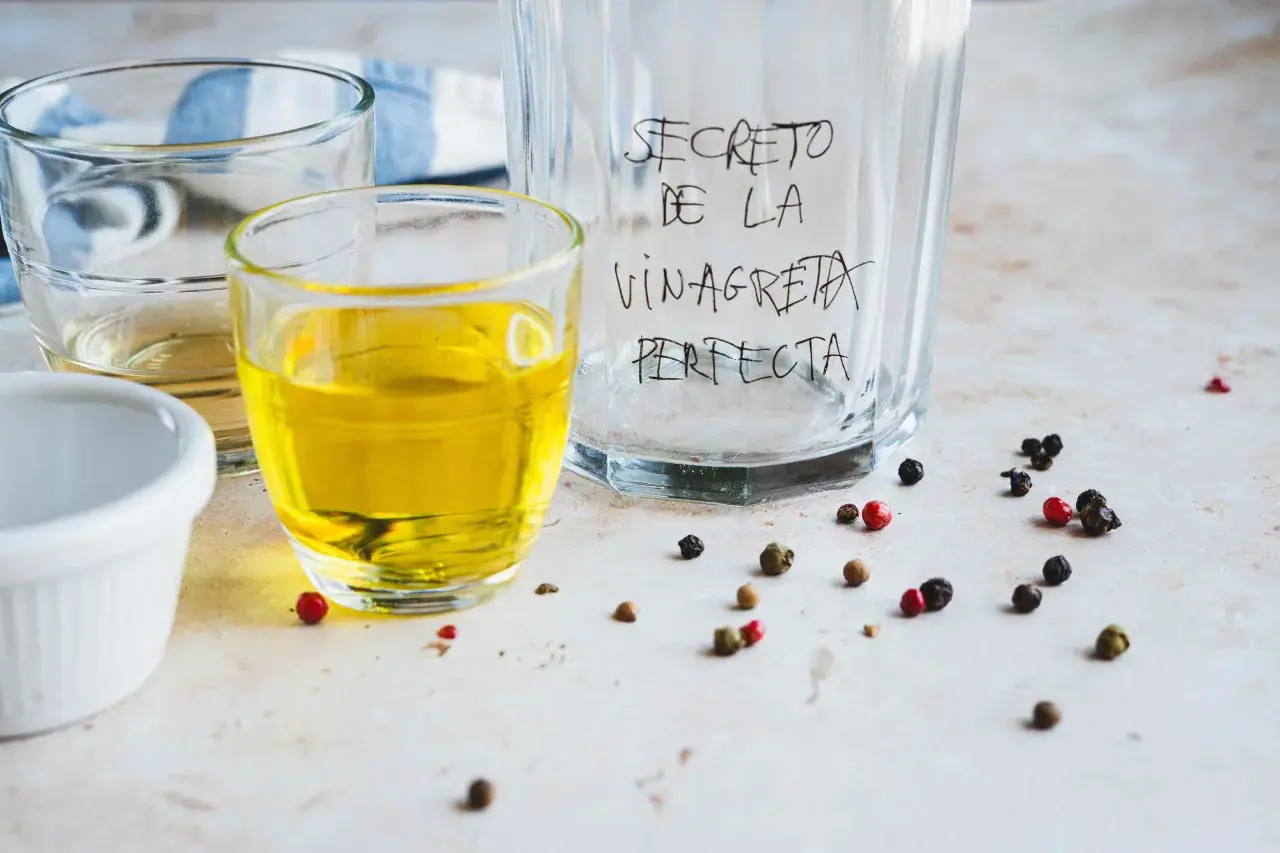 Ingredientes para la receta de vinagreta perfecta: aceite, vinagre y granos de pimienta.
