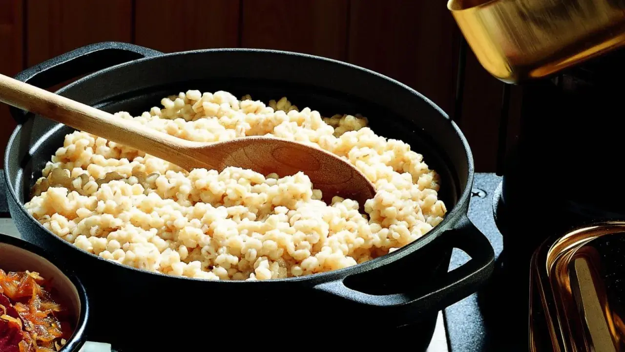 Un mestolo di legno affonda in una pentola piena di fumante orzo perlato, pronto per essere servito.