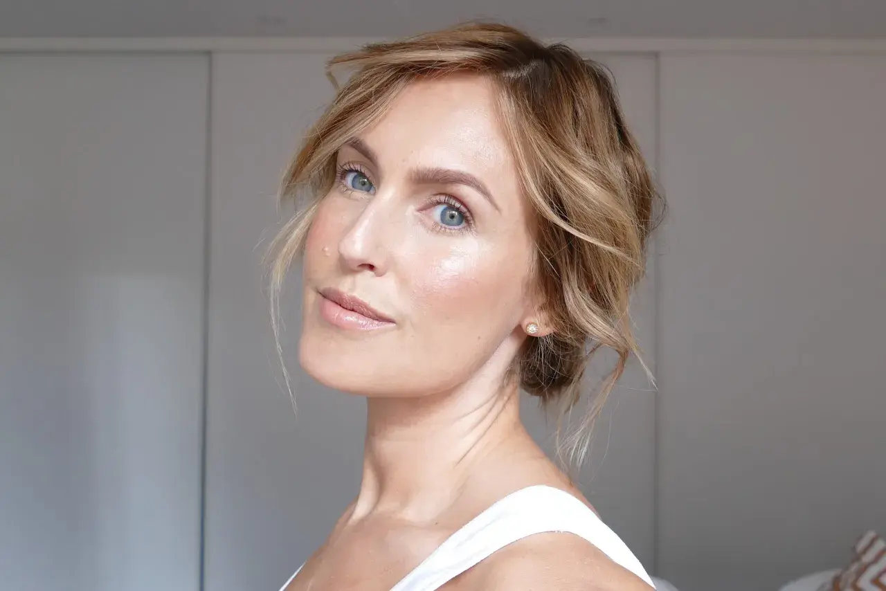 En kvinna med blå ögon och blont hår visar hur man får glow i ansiktet med naturlig makeup och lyster.