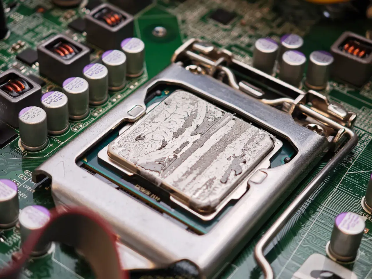 Procesor z zaschniętą pastą termoprzewodzącą, gotowy do testu chłodzenia CPU. Widoczne kondensatory i elementy płyty głównej.