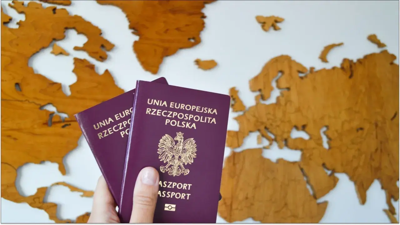 Dłoń trzyma dwa polskie paszporty na tle drewnianej mapy Europy. Czas na podróż!