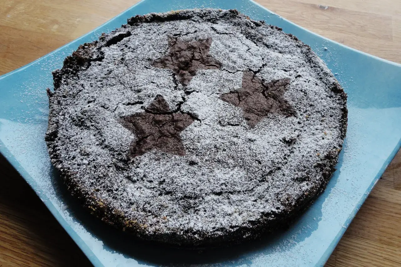 En härlig glutenfri kladdkaka med stjärnmönster av florsocker på en blå tallrik.