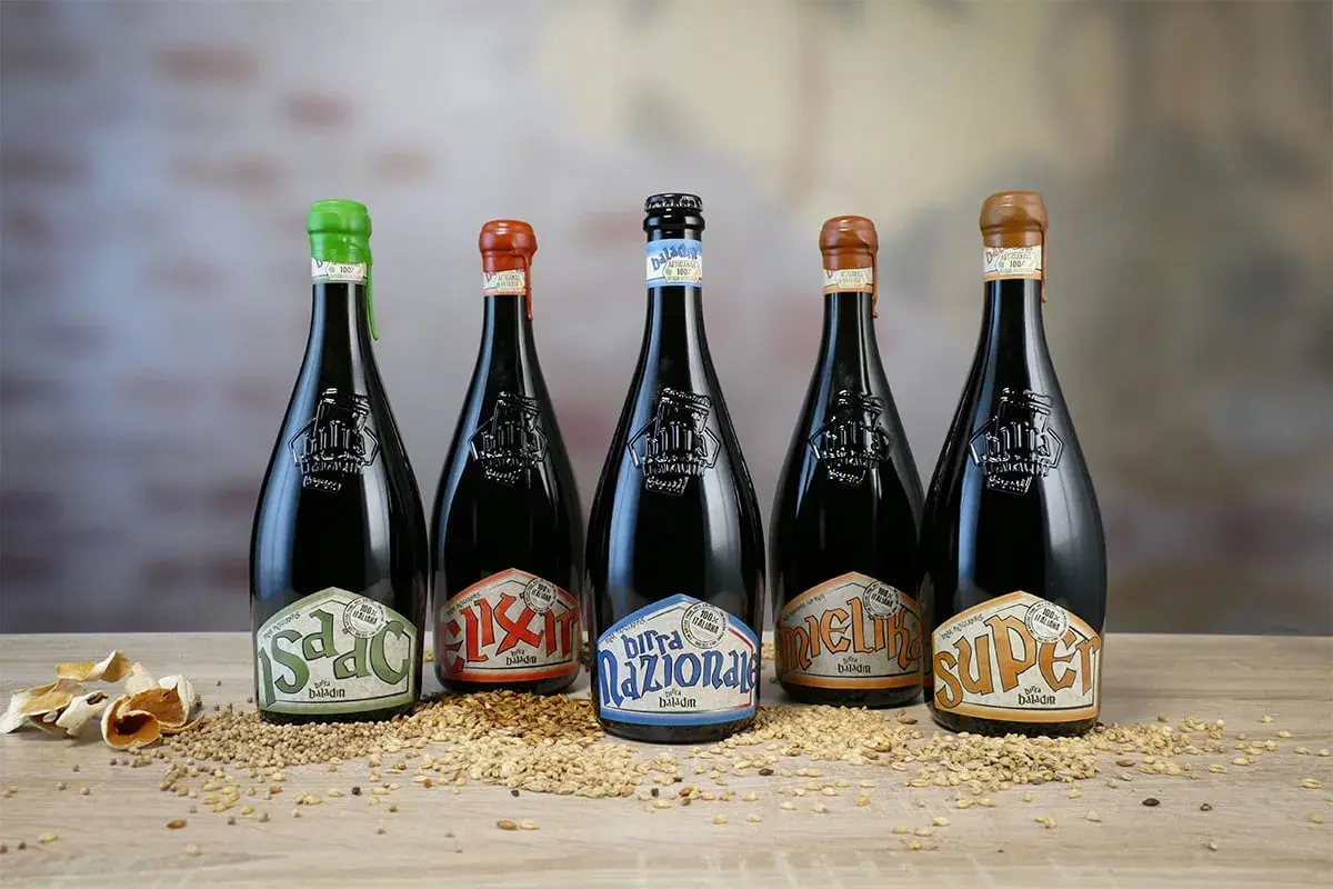 Cinque bottiglie di birra Baladin, tra le migliori birre artigianali italiane, disposte su un letto di cereali.