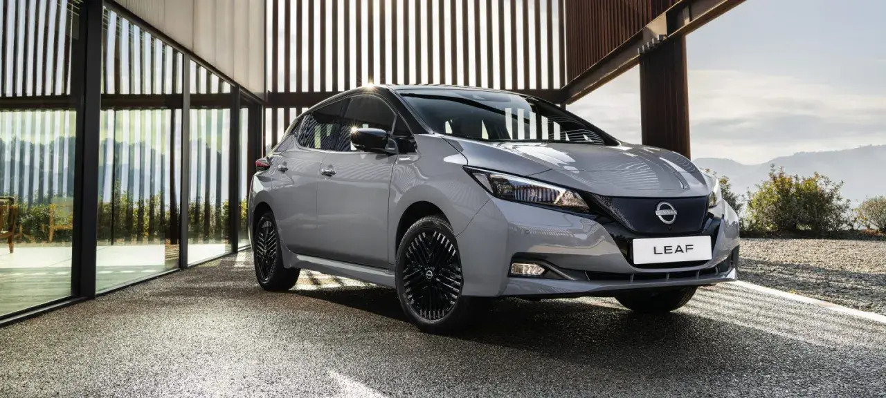 Szary Nissan Leaf stoi przed nowoczesnym budynkiem z przeszklonymi ścianami.
