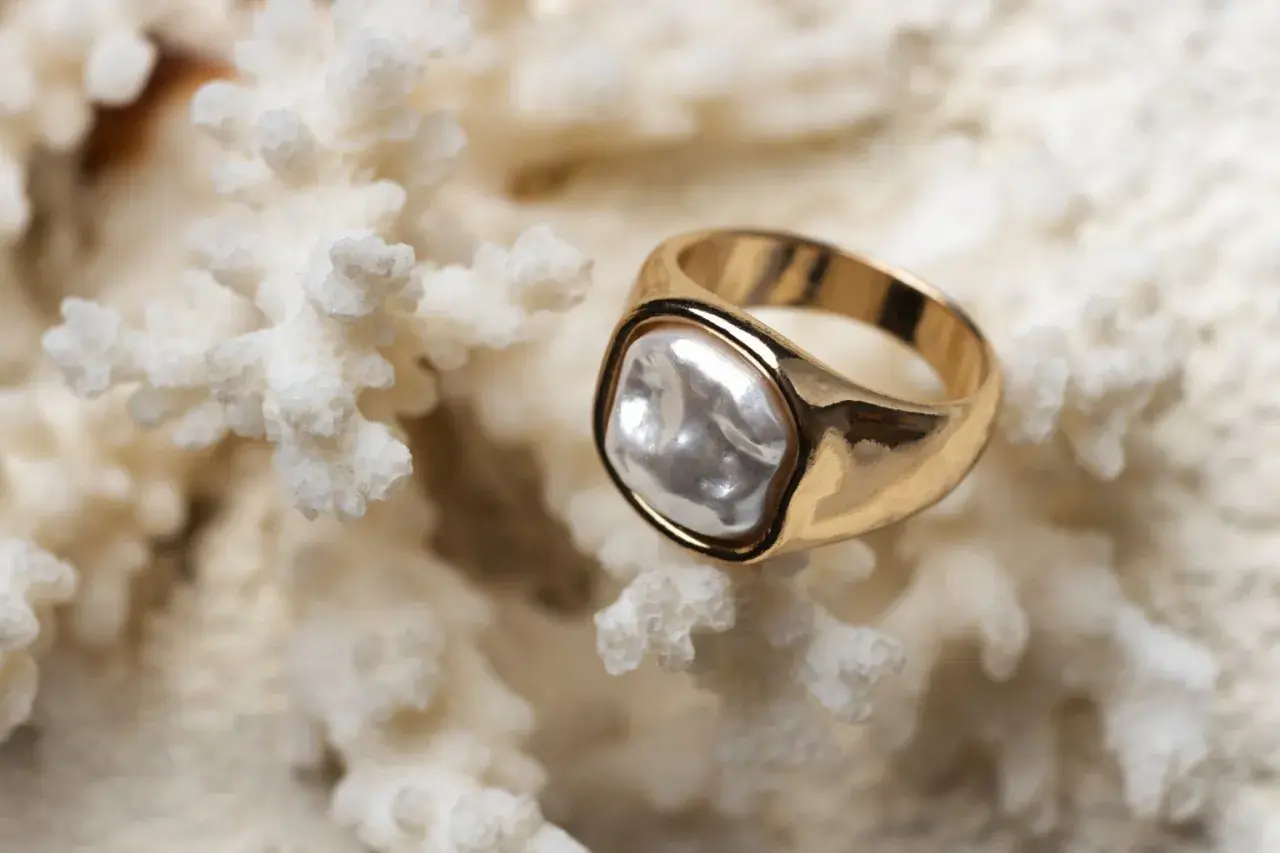Anillo de oro amarillo con perla irregular sobre coral blanco. La diferencia entre oro blanco y oro amarillo es evidente en su brillo.