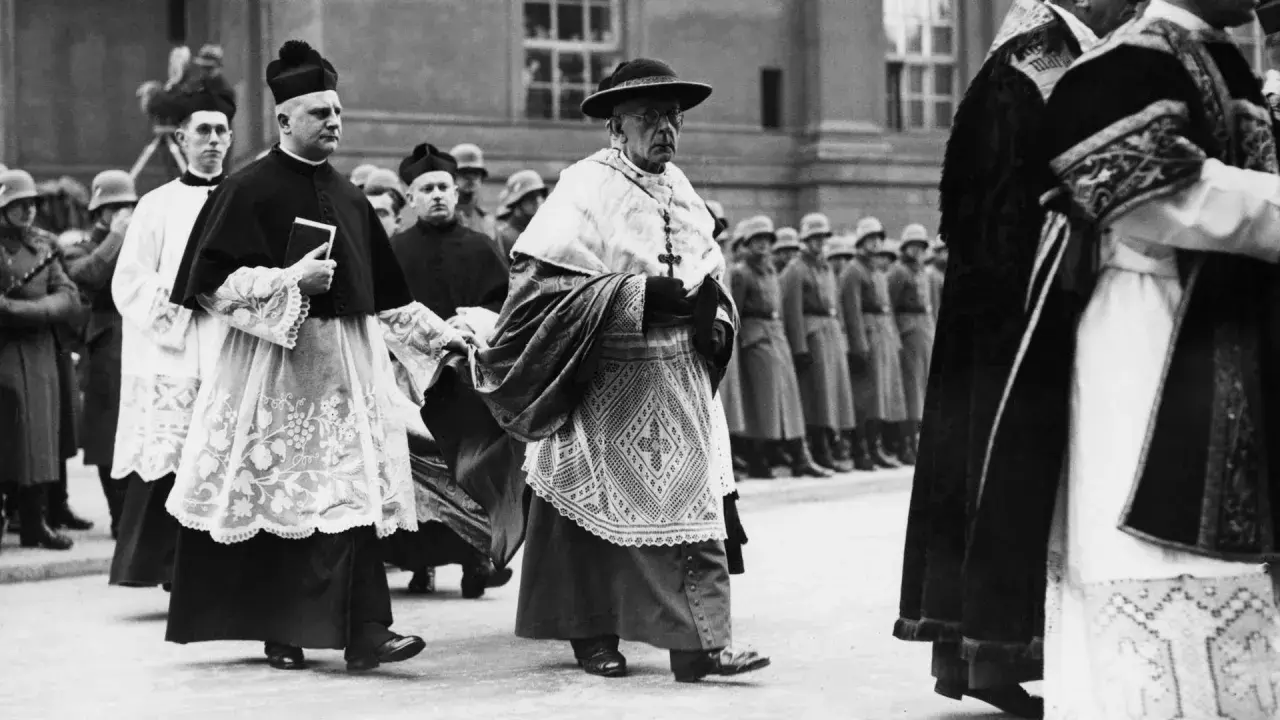 Geistliche in feierlicher Kleidung marschieren, im Hintergrund Soldaten. Die Kirchensteuer im Nationalsozialismus war ein komplexes Thema.