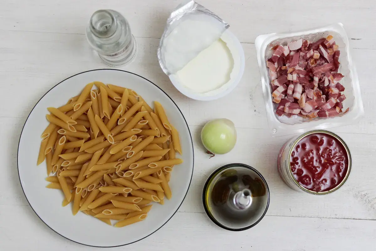 Penne, boczek, śmietana, cebula, oliwa, pomidory z puszki na białym tle.