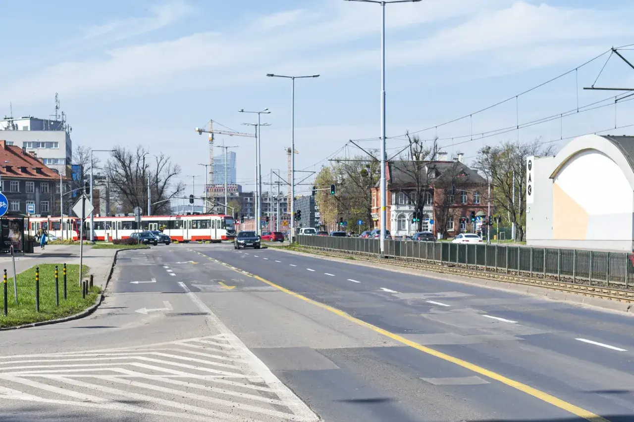 Ulica z tramwajem, samochodami i budynkami w tle.