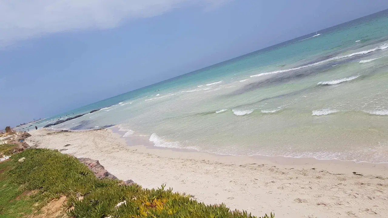 Piękne djerba plaże z turkusową wodą i białym piaskiem. W oddali widać kilka osób kąpiących się w morzu.