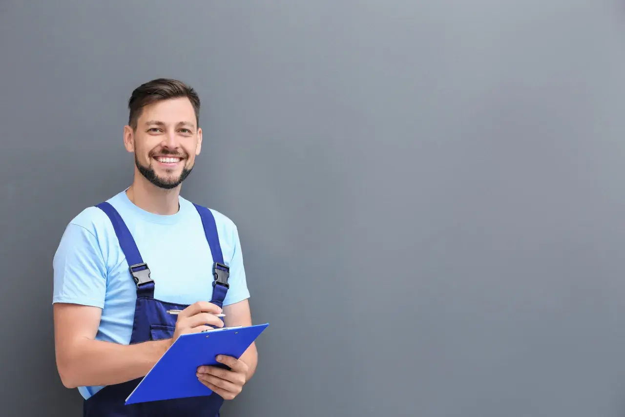 Técnico sonriente con mono azul y camiseta clara, escribiendo en una carpeta azul. Listo para limpiar aire acondicionado.