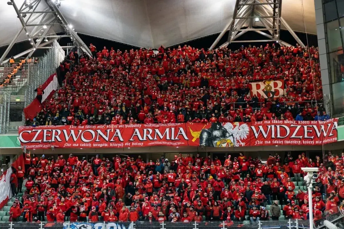 Tłum kibiców Widzewa w czerwonych barwach, z transparentem "Czerwona Armia Widzewa".