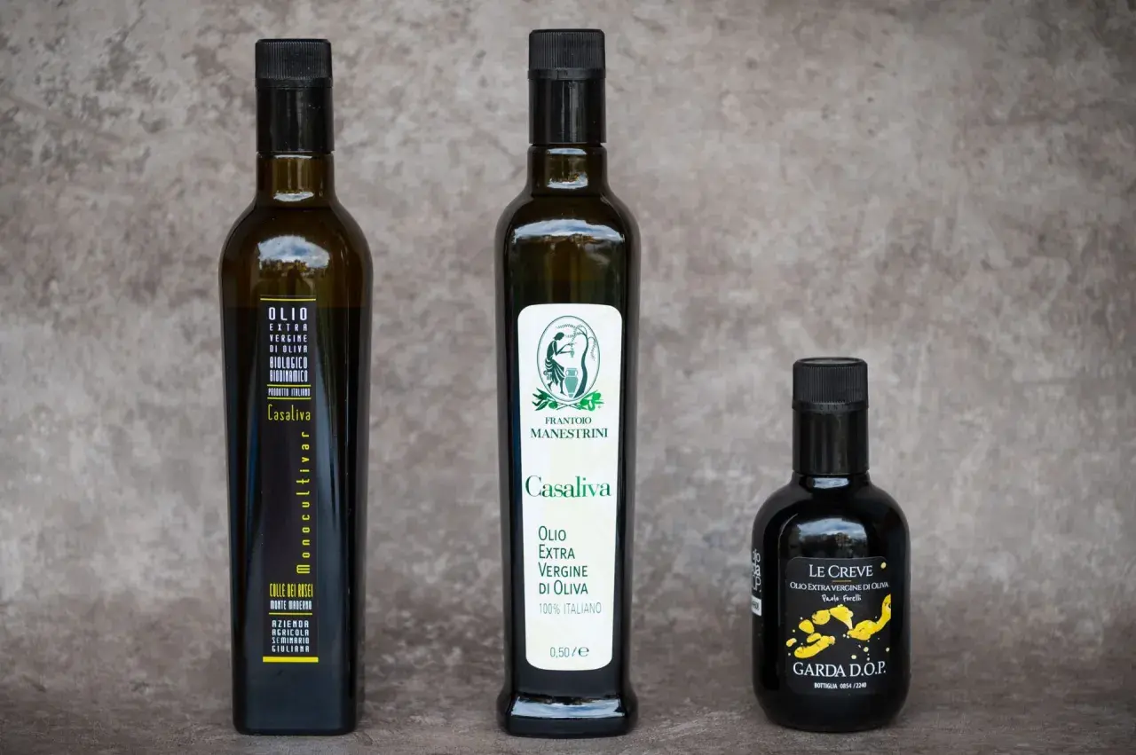 Tre bottiglie di olio extra vergine d'oliva, tra cui un Casaliva monocultivar e uno con etichetta "Le Creve Garda D.O.P.".